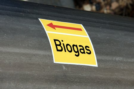 Nahaufnahme eines silbernen großen Rohrs mit einem gelben Aufkleber darauf. Auf dem Aufkleber steht zeigt ein Pfeil nach links und darunter steht Biogas