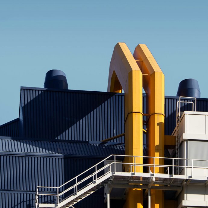 [Translate to English:] Ein Industriegebäude von außen fotografiert an dem 2 große gelbe Rohre hinauf laufen
